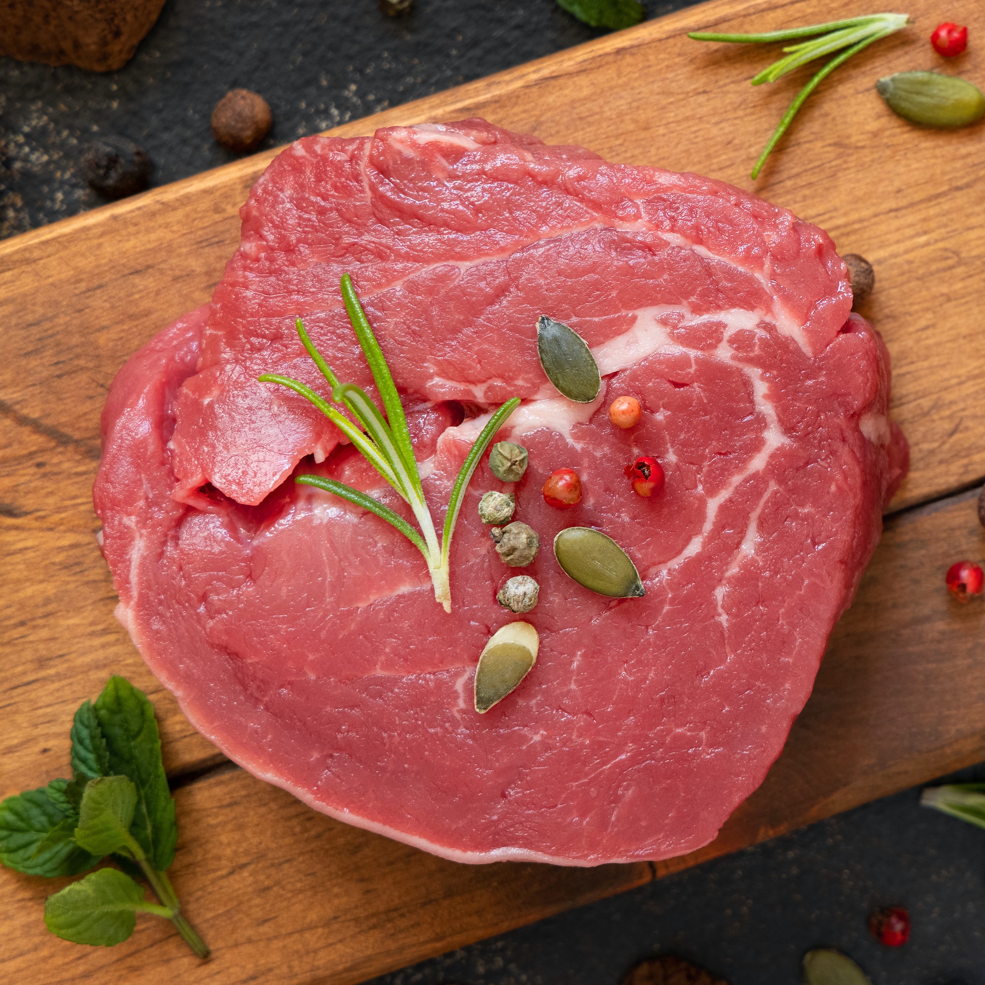 Raw beef fillet steak with herbs and spices on wooden board on dark table top view